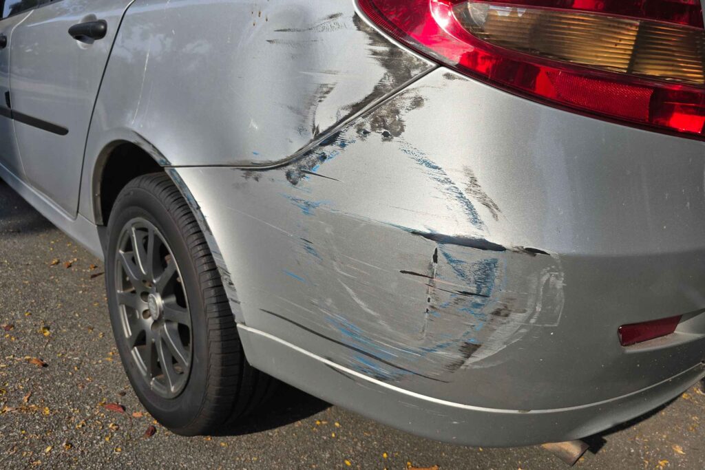 Scratched bumper and side dent on a silver car in an article on who pays for a rear-end collision in Texas.