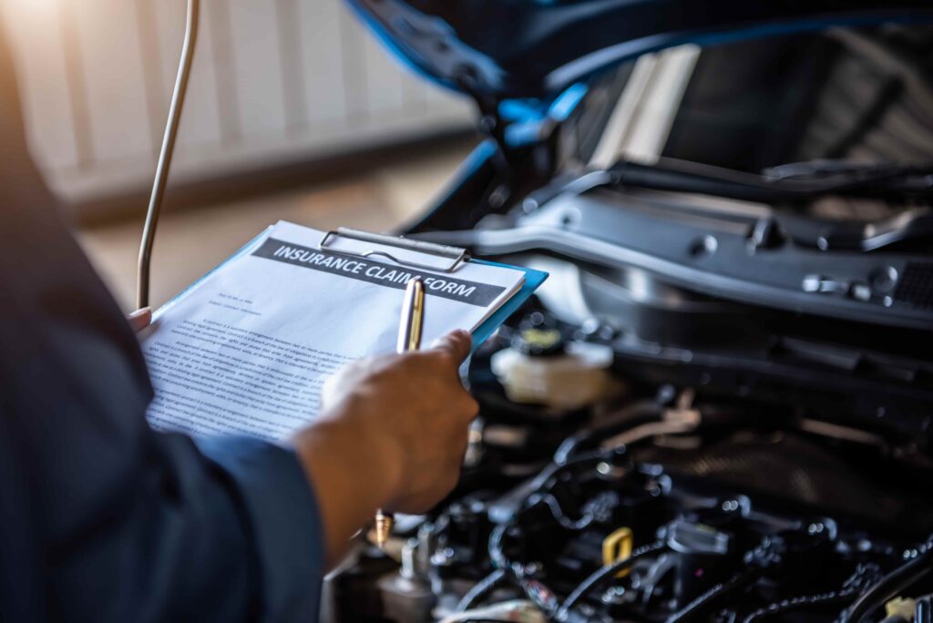 Insurance adjuster inspecting car engine while reviewing auto insurance claim form for vehicle damage assessment.