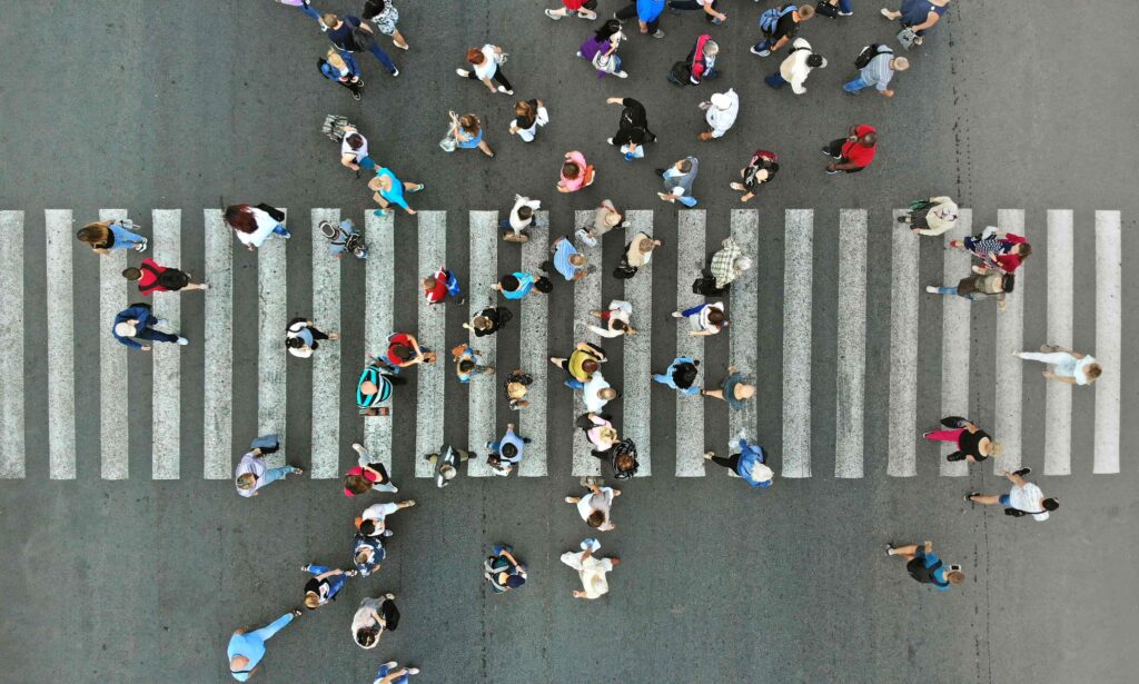 Aerial view of large group of pedestrians crossing a busy city crosswalk, highlighting pedestrian traffic, urban mobility, and road safety. Aerial view of large group of pedestrians crossing a busy city crosswalk, highlighting pedestrian traffic, urban mobility, and road safety.