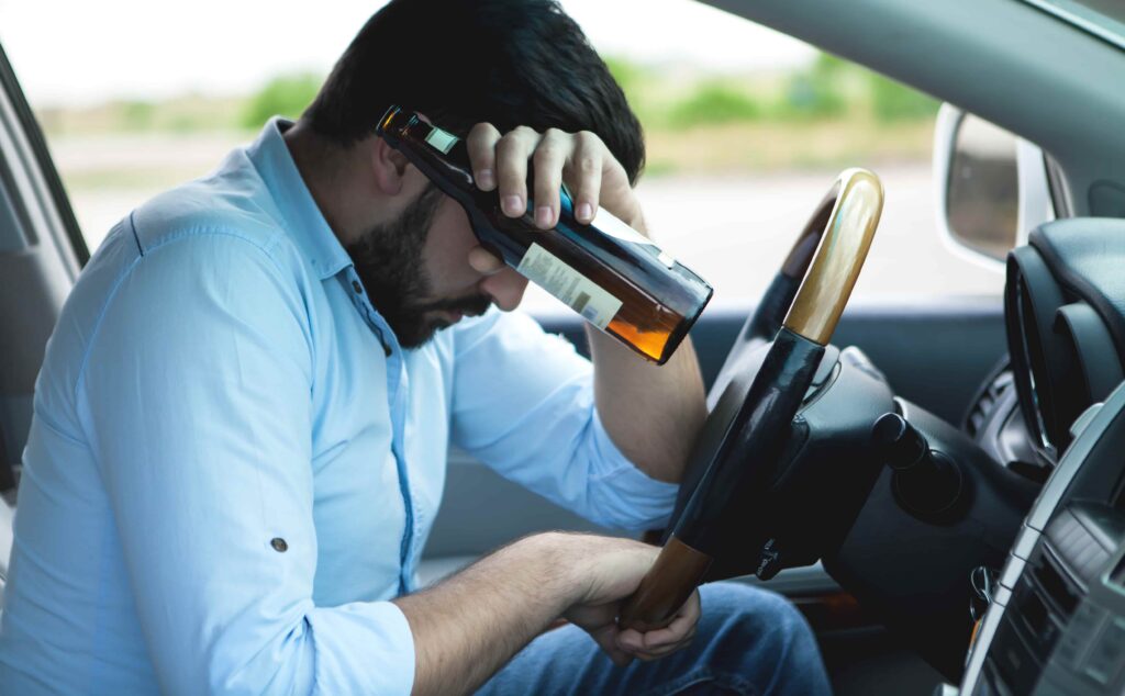 Intoxicated driver sitting in a car holding a beer bottle, illustrating drunk driving and impaired driving risks. Intoxicated driver sitting in a car holding a beer bottle, illustrating drunk driving and impaired driving risks.