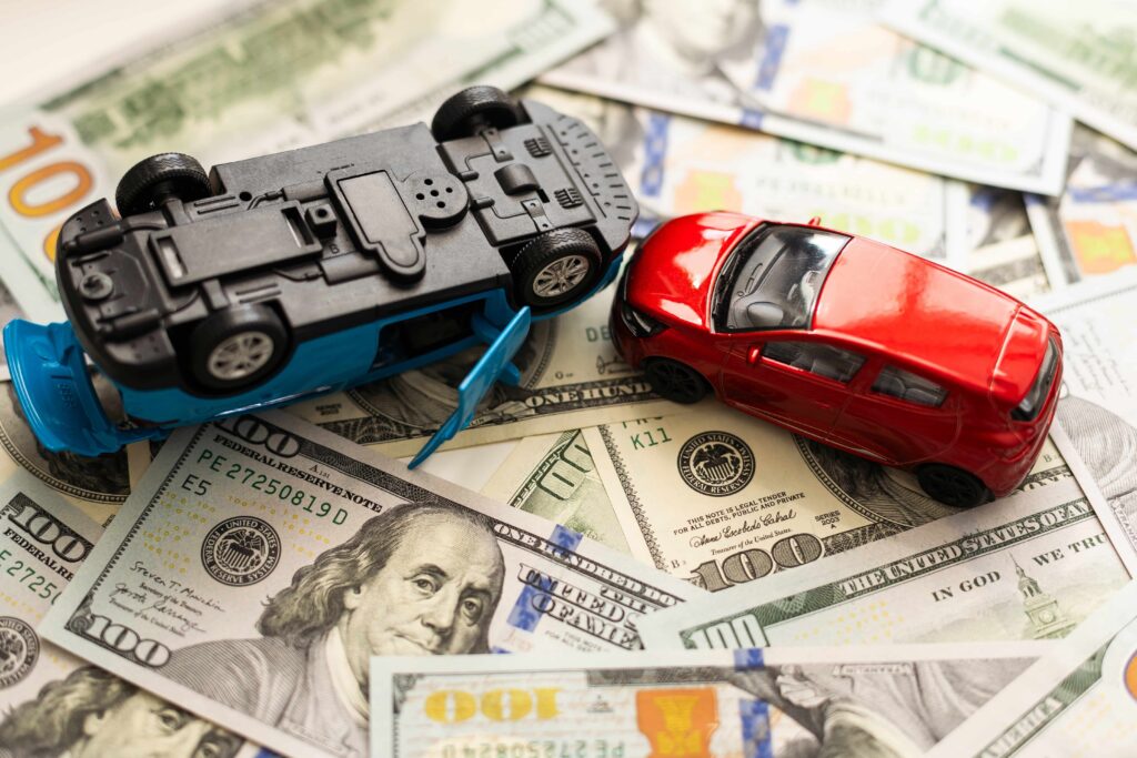 Toy cars in a collision on US dollar bills symbolizing car accident costs, insurance claims, and financial compensation.