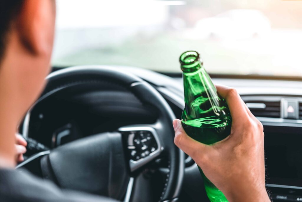 Driver holding a beer bottle while behind the wheel, illustrating the dangers of drinking and driving.