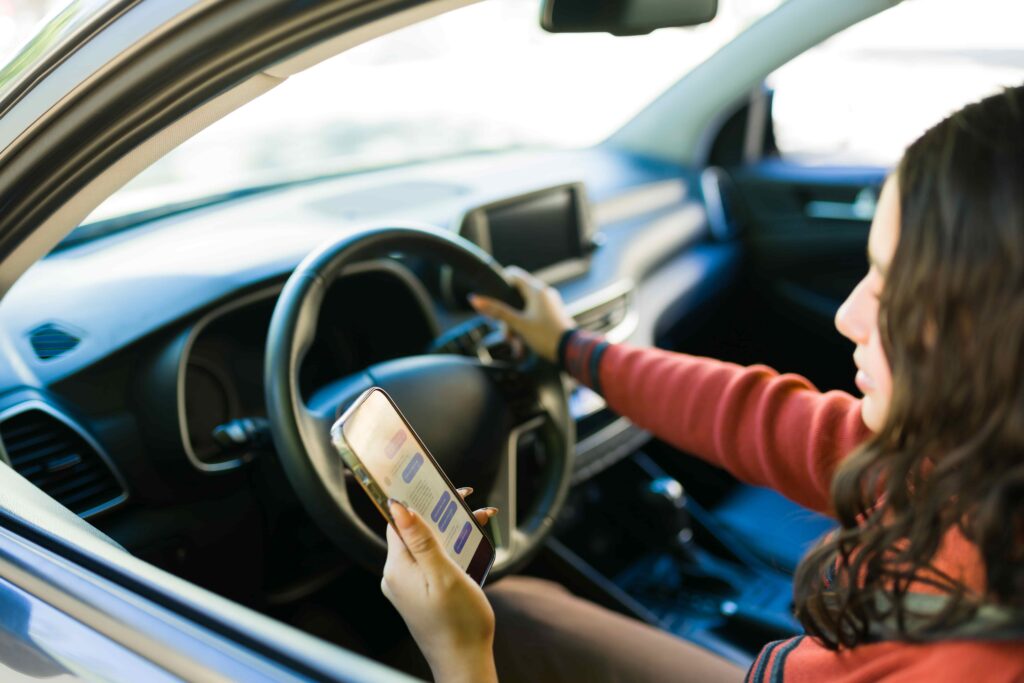 Woman using smartphone while driving a car, demonstrating distracted driving and texting behind the wheel.