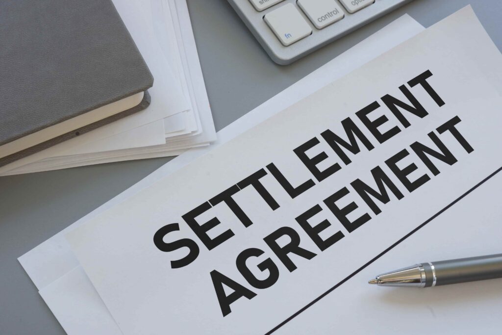 Settlement agreement document on a desk with pen and paperwork representing legal settlement or lawsuit resolution.