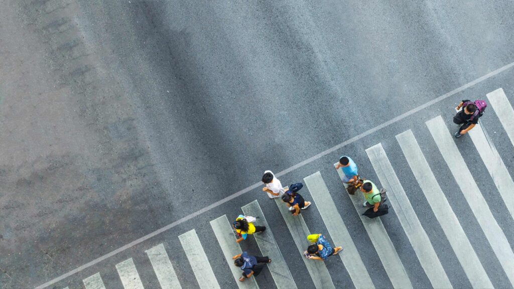 Aerial view of pedestrians walking across a marked crosswalk at city intersection, highlighting pedestrian safety and urban traffic awareness. Aerial view of pedestrians walking across a marked crosswalk at city intersection, highlighting pedestrian safety and urban traffic awareness.