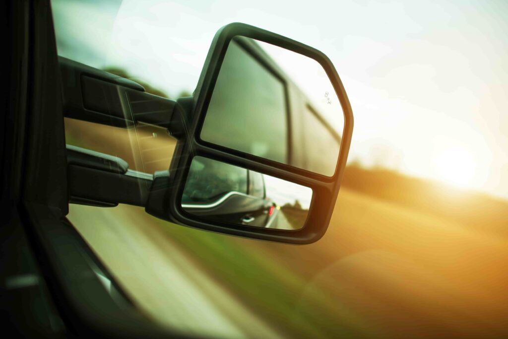 Close-up of a truck&rsquo;s side mirror reflecting the road and traffic behind, highlighting commercial vehicle visibility and driving safety.