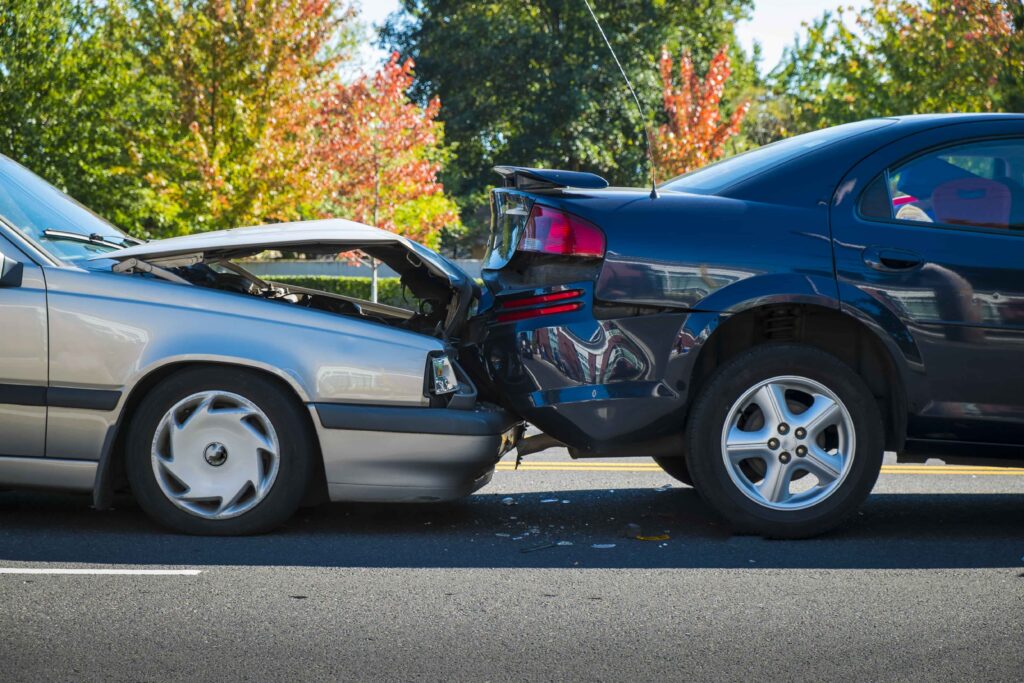 Rear-end car collision with visible vehicle damage on city street, illustrating traffic accident and auto insurance claim scenario