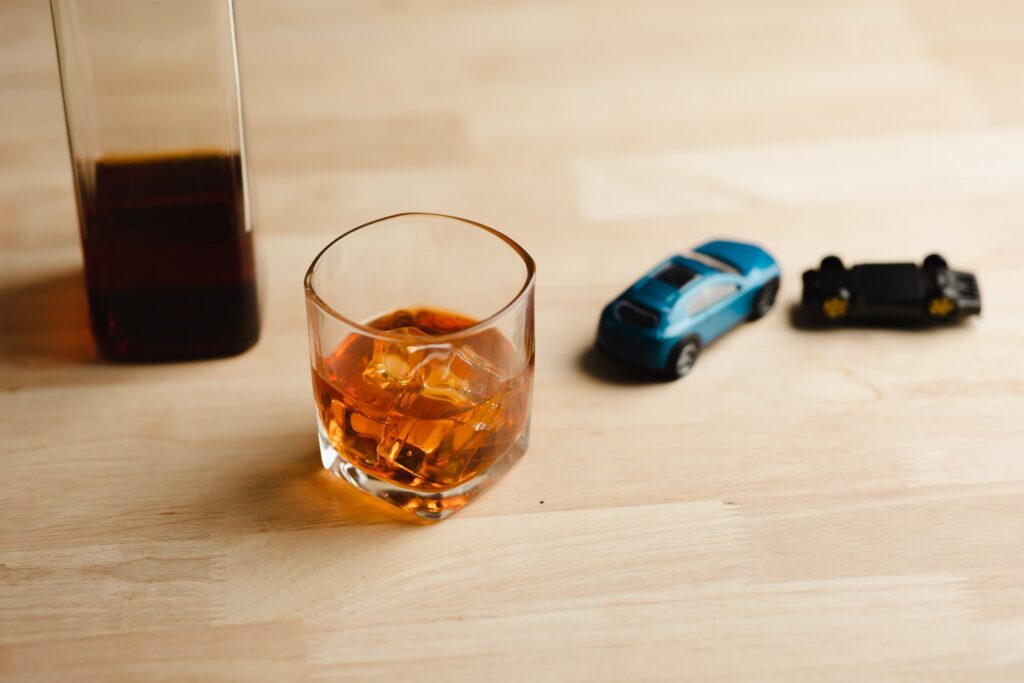 Alcohol bottle and toy cars representing criminal DWI charges versus civil injury lawsuits in Texas involving drunk driving accident claims and damages