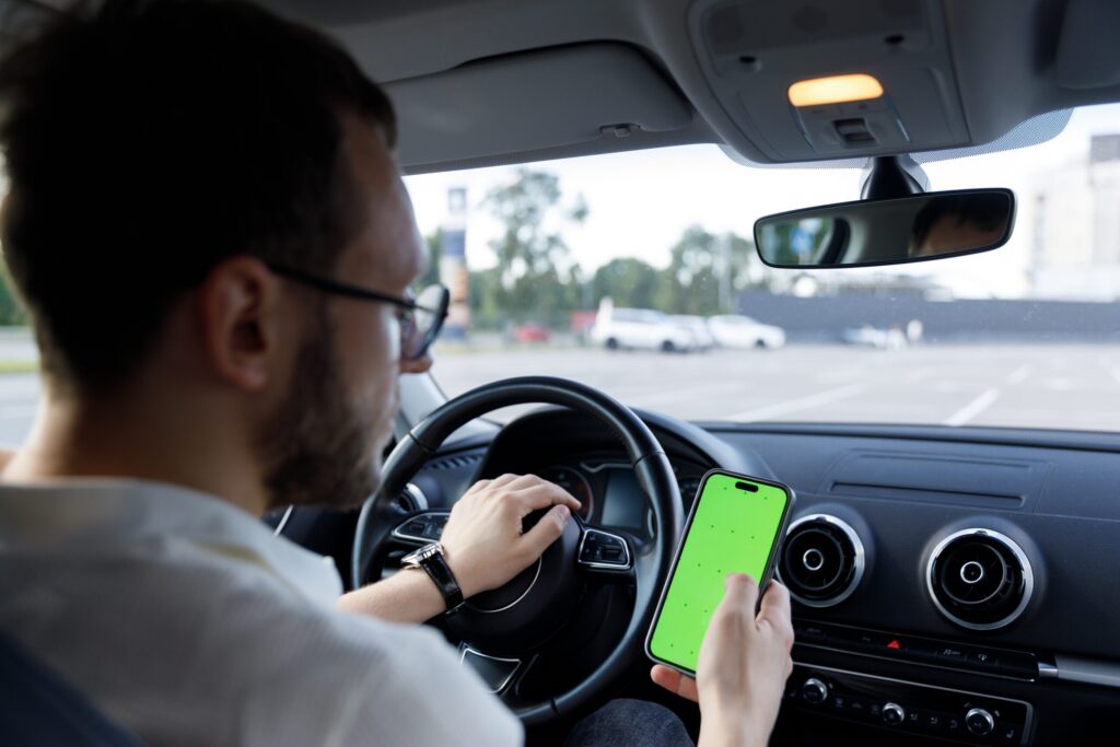 Texas rideshare driver looking at a smartphone behind the wheel, illustrating distracted driving accidents involving Uber and Lyft vehicles