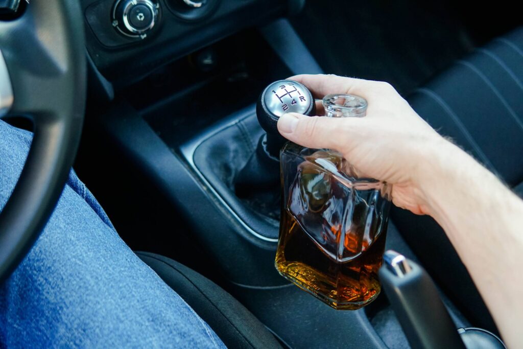 Driver holding a liquor bottle inside a vehicle before a crash, highlighting the dangers handled by a Texas drunk driving accident lawyer after serious DUI accidents