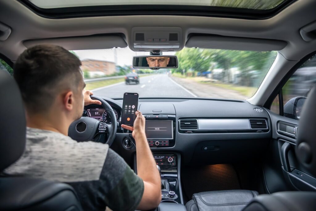 An over-the-shoulder view of a man holding a smartphone while driving, showing an example of negligence for Texas Distracted Driving Accident Lawyers.