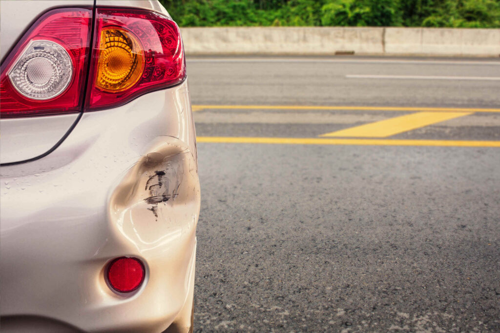 A close-up of a dented rear bumper on a silver car parked by a highway, showcasing property damage handled by Texas Hit and Run Accident Lawyers.