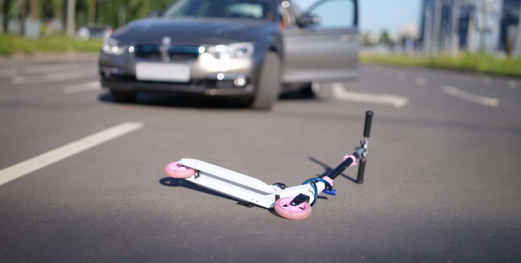 A white and pink toy scooter lies on the pavement in front of a stopped car, showing a collision scene if your child was injured in a Texas car accident.