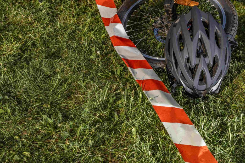 A bicycle helmet and wheel behind red safety tape on the grass represent evidence handled by San Antonio Bicycle Accident Lawyers.