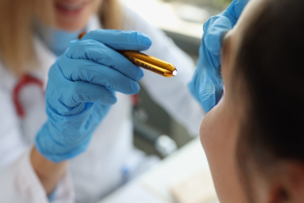 Doctor in blue gloves shining a penlight into a patient's eye during an exam.