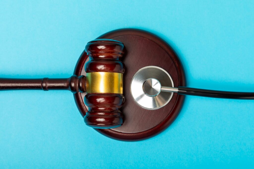 Wooden gavel resting on a sounding block alongside a stethoscope on a blue background.