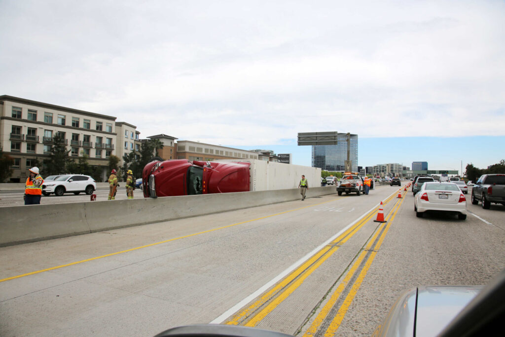 An overturned red semi truck on a highway barrier illustrates major highway crashes handled by Texas Truck Accident Lawyers.