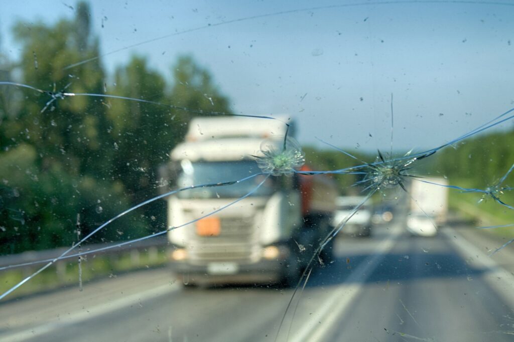 A cracked windshield looking out at a large semi truck on the highway illustrates what to do after a truck accident in College Station.