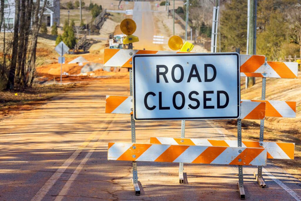 A road closed sign with orange construction barriers highlights hazards that cause work zone car accidents on San Antonio highways.