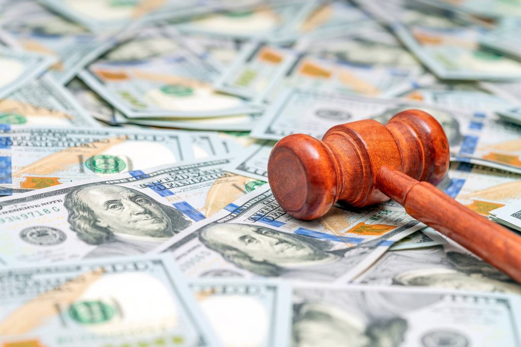 Wooden judge gavel resting on top of a pile of hundred dollar bills.