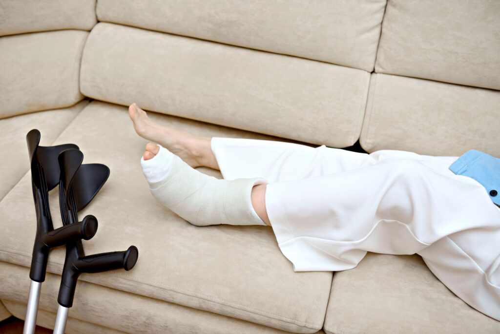 Person resting on a sofa with a bandaged leg cast next to a pair of crutches.