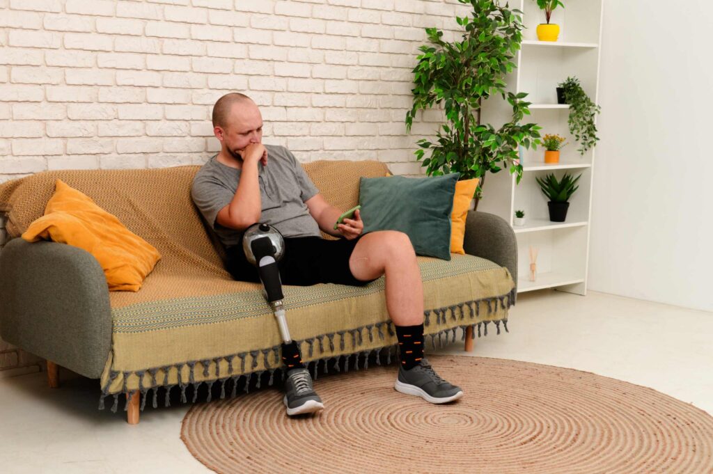 Man with a prosthetic leg sitting on a couch while looking at his smartphone.